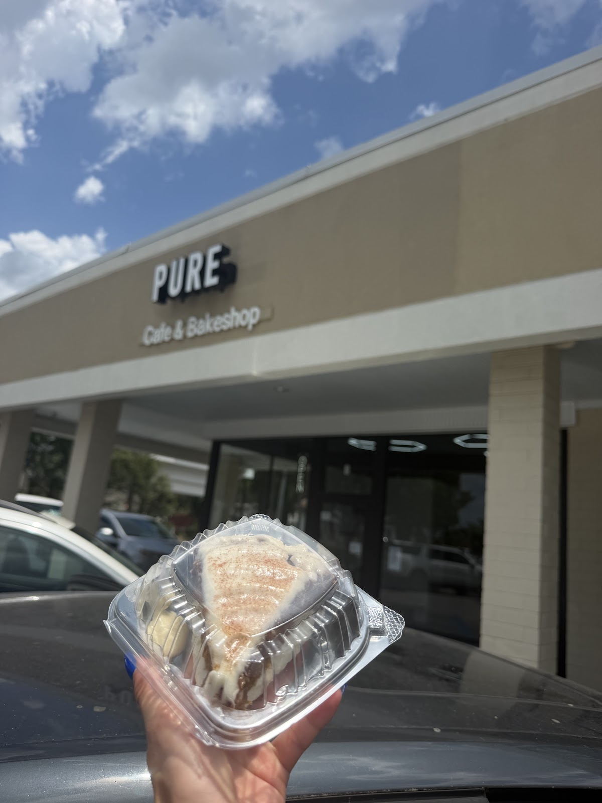 Packaged iced baked good held in front of the Pure Cafe and Bakeshop storefront